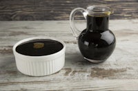 a pitcher of black sauce next to a white bowl